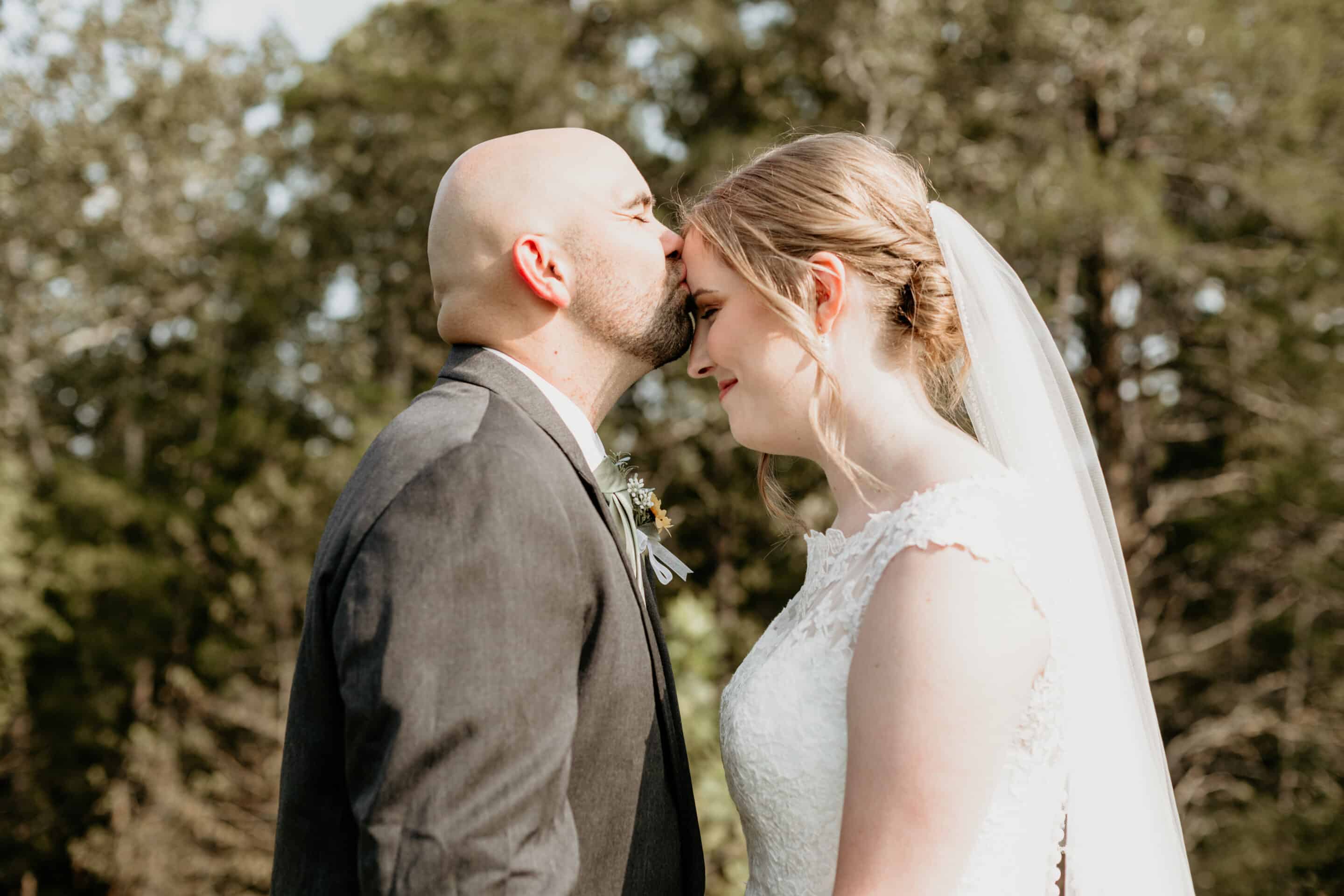 Groom kisses bride on the forehead during outdoor wedding portraits in Kansas City Missouri
