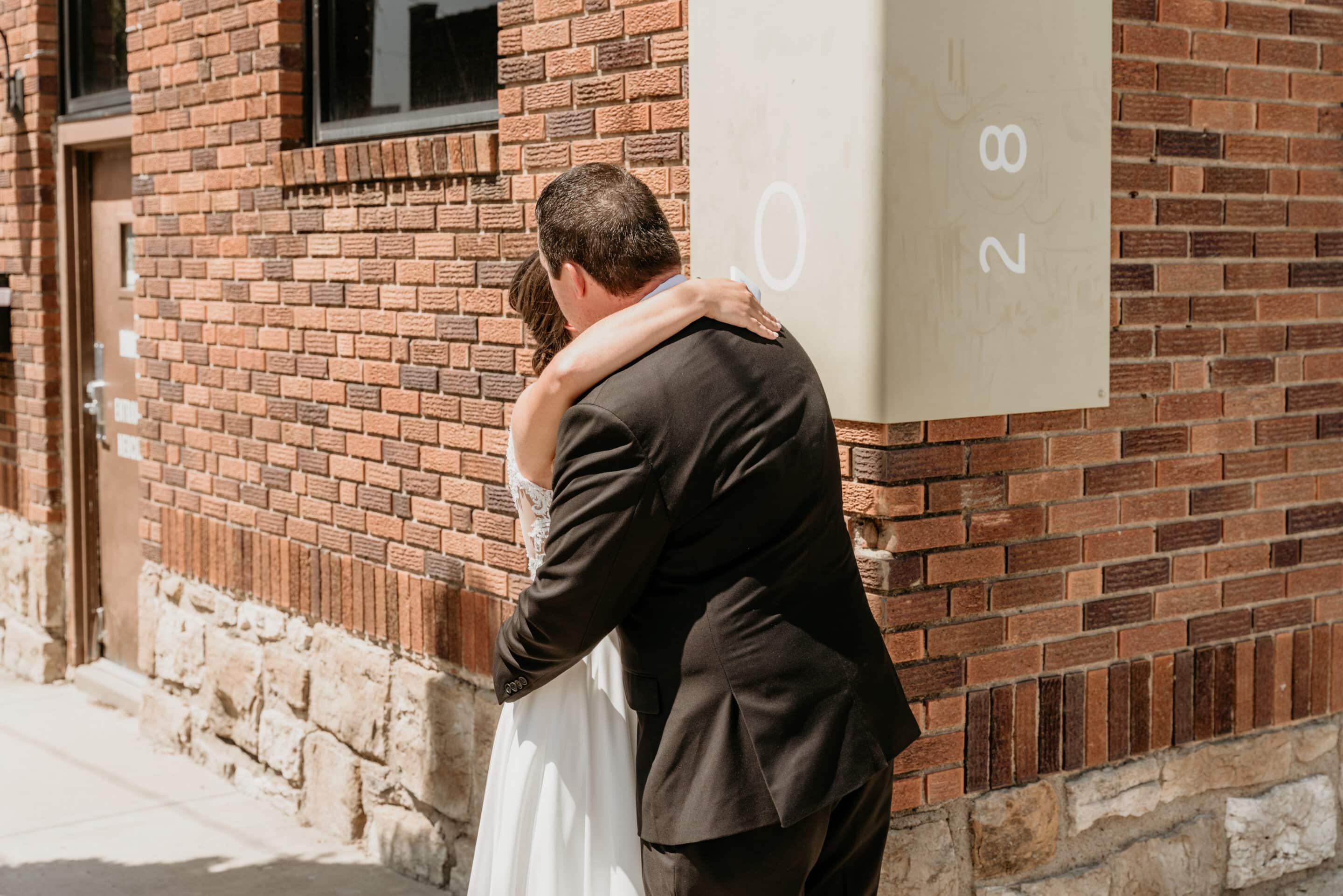 Bride and groom embrace during first look against brick wall in Downtown Kansas City Missouri wedding
