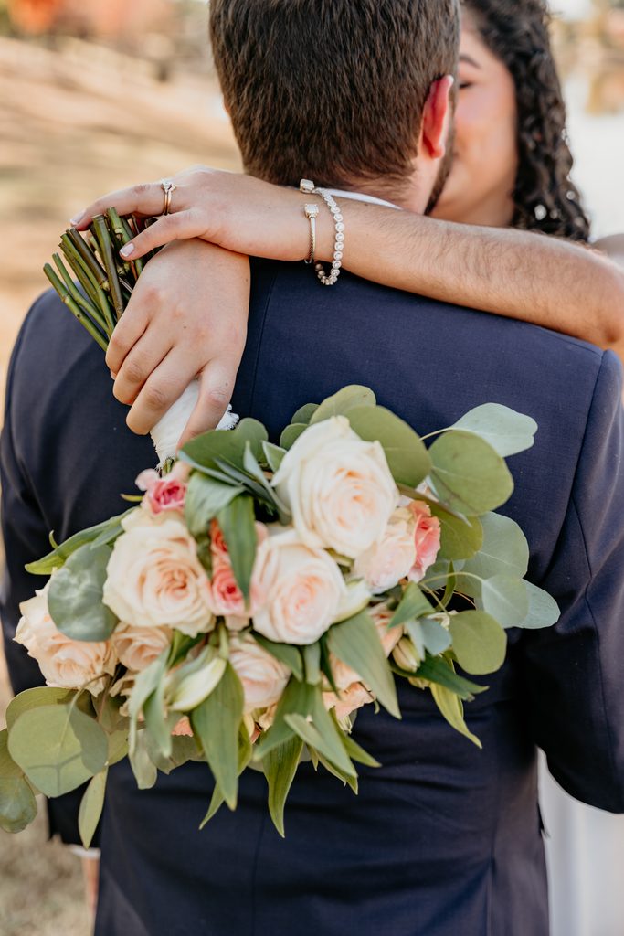 Couple embracing on rocks at the water's edge, the bride in a flowing white dress, during an intimate Kansas City elopement
