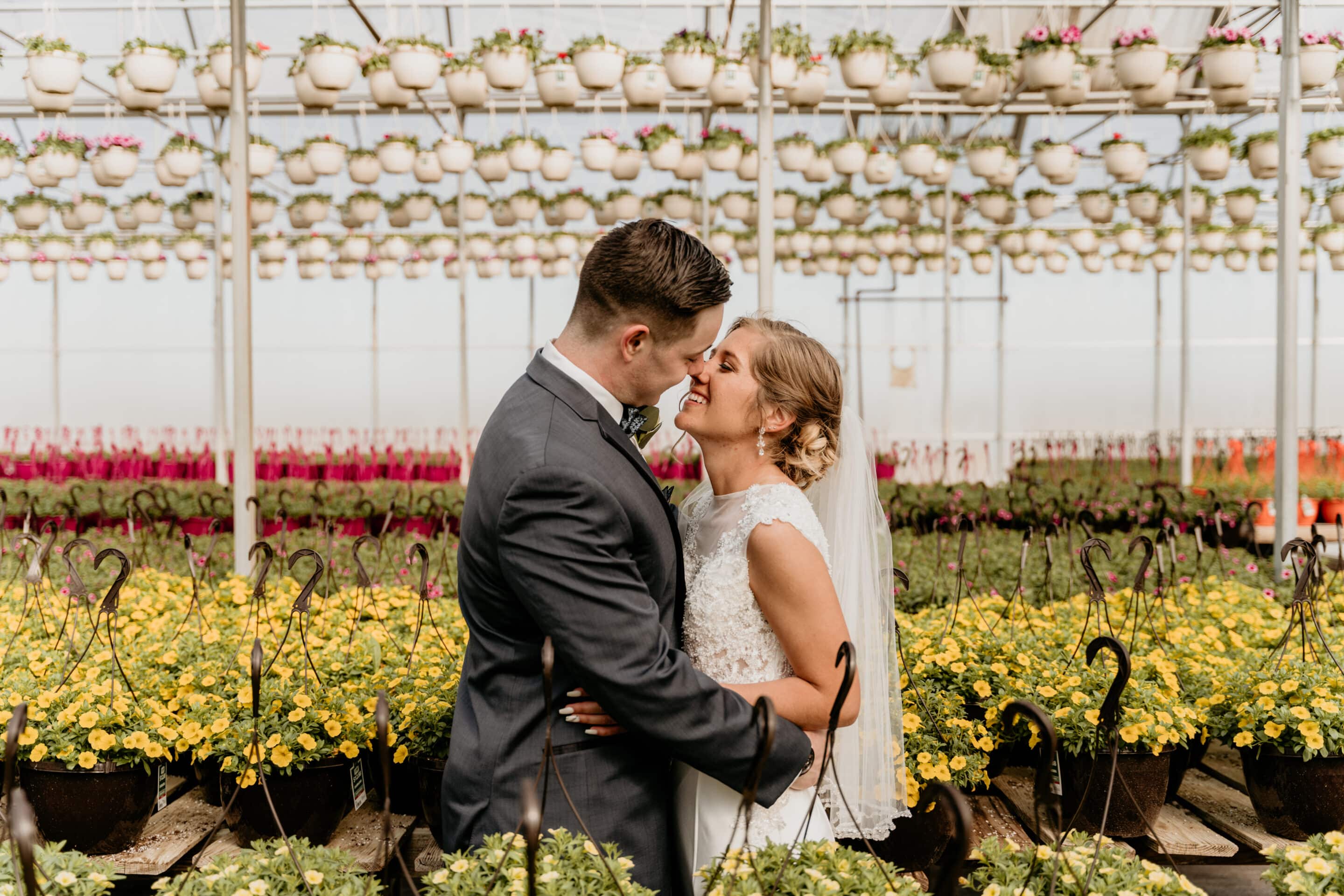Bride and groom embrace among hanging baskets and yellow flowers in greenhouse wedding in Kansas City Missouri
