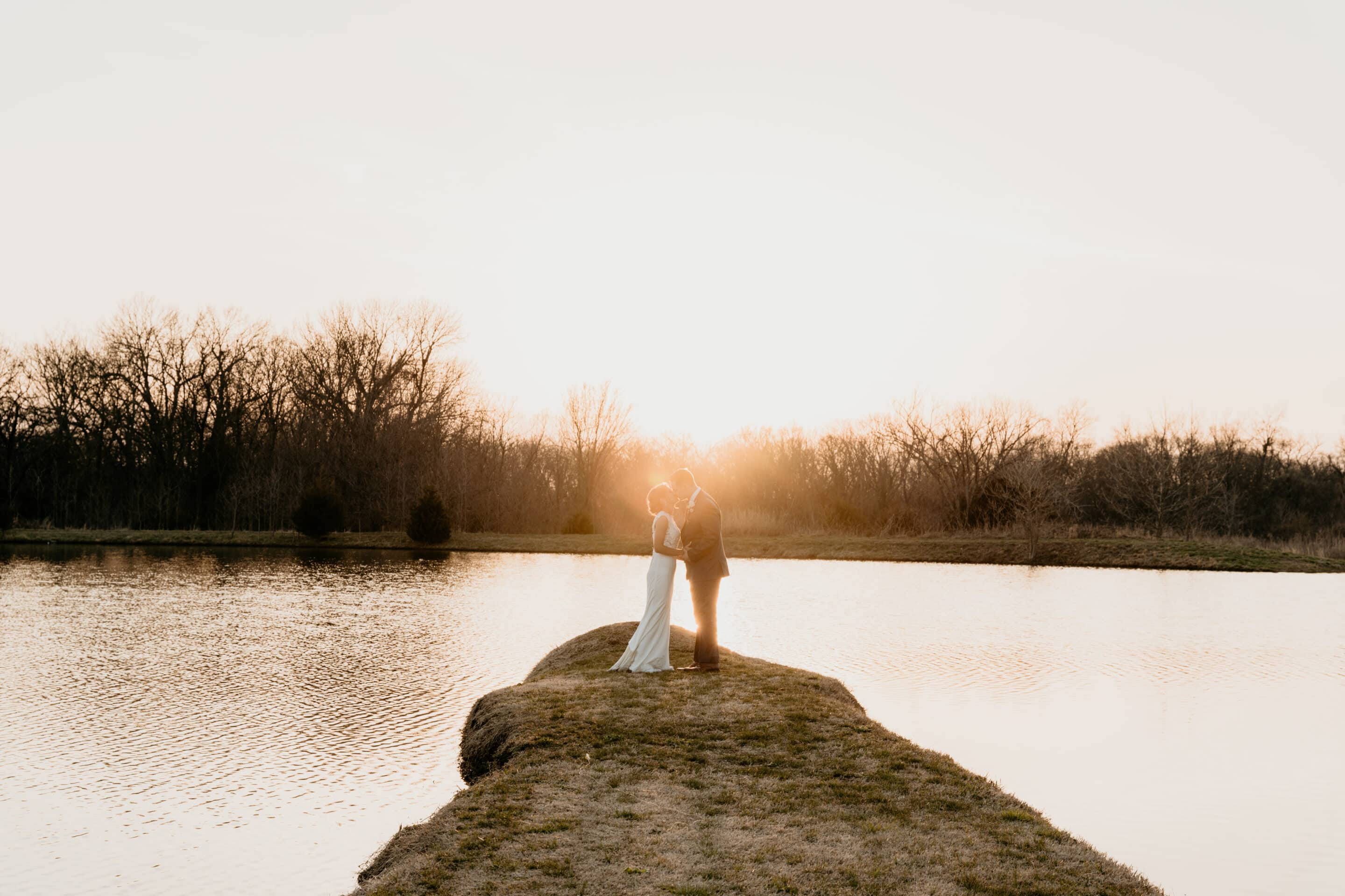 Bride and groom silhouetted at golden hour sunset beside pond at Kansas City Missouri wedding venue