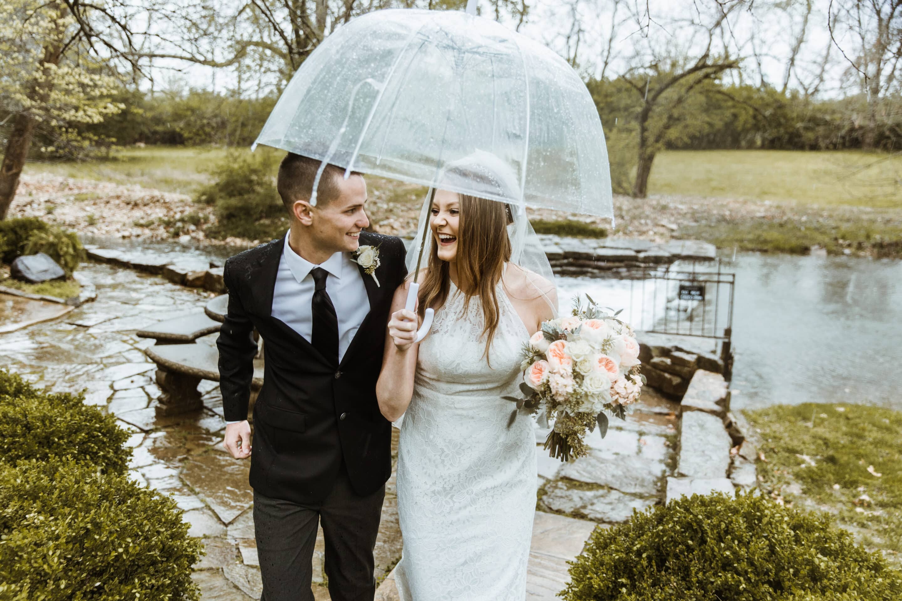 Bride and groom laugh under clear umbrella during rainy outdoor elopement in Kansas City Missouri