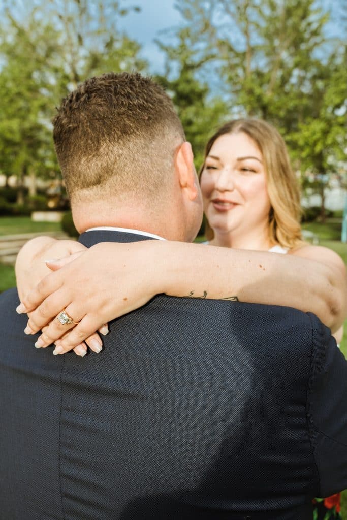 Bride-to-be smiles over her fiance's shoulder while hugging him after the proposal at the Nelson-Atkins in Kansas City