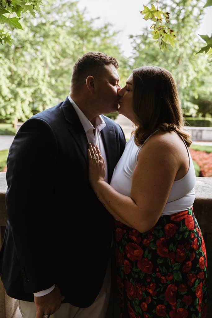Engaged couple shares a kiss in front of the trees at the Nelson-Atkins in Kansas City