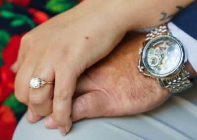 Close-up of a woman's hand wearing a new solitaire engagement ring as she holds her partner's hand above his silver wristwatch