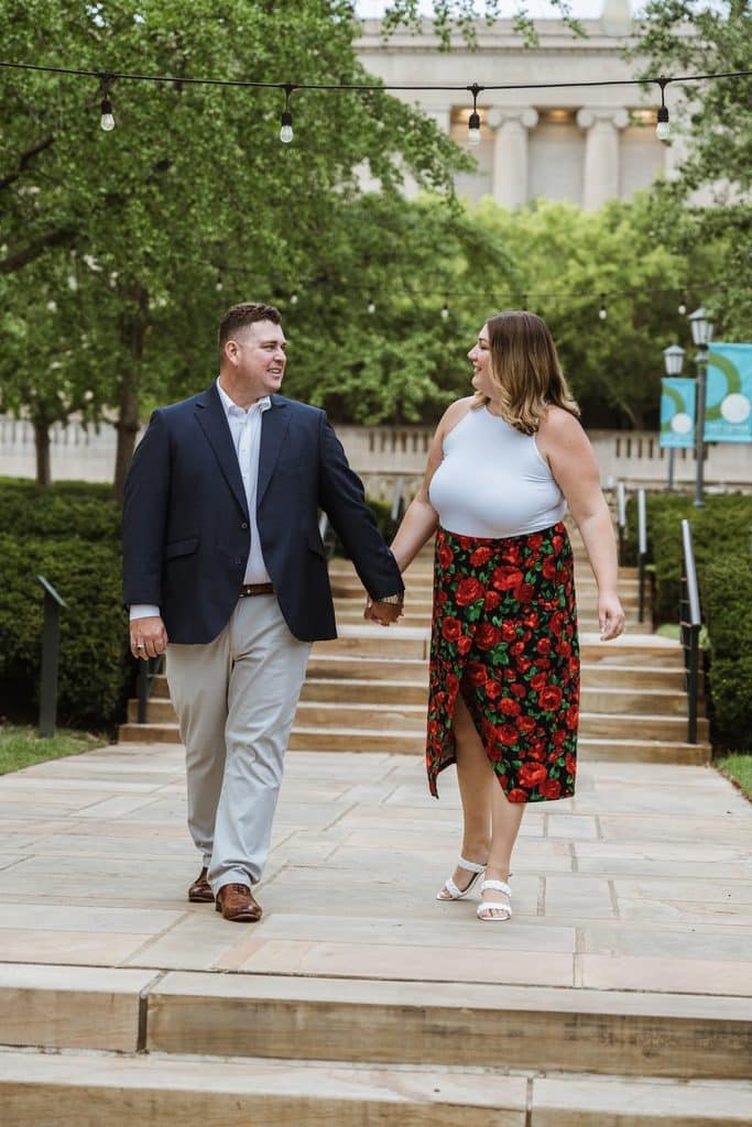 Engaged couple walks down the stone steps south of the Nelson-Atkins Museum of Art in Kansas City