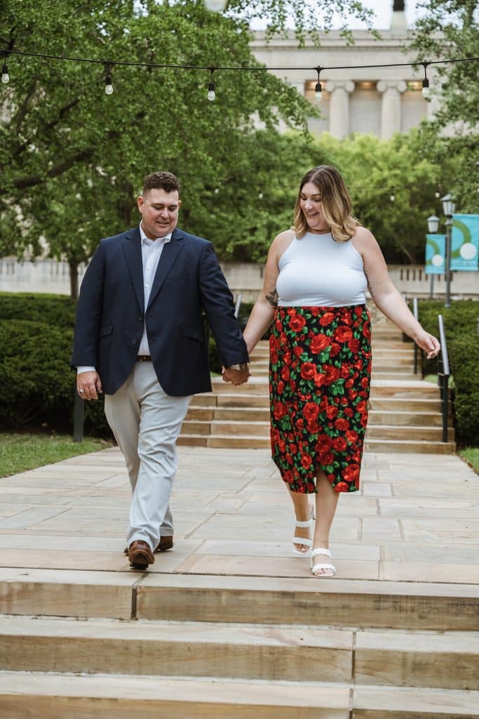Engaged couple holds hands walking down the stone steps at the Nelson-Atkins Museum of Art in Kansas City