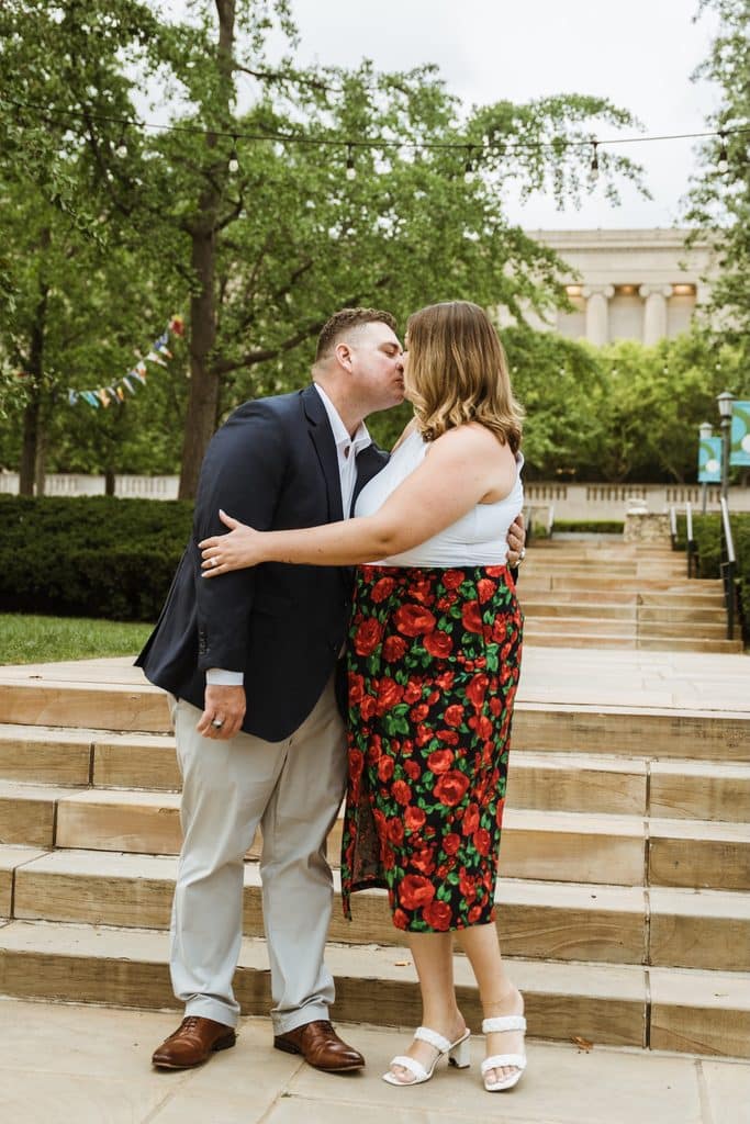 Groom-to-be kisses his fiancee's cheek at the base of the stone steps at the Nelson-Atkins in Kansas City
