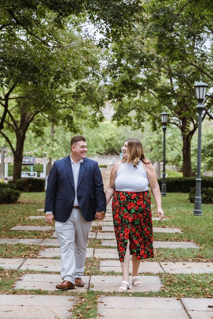 Engaged couple walks toward the camera on the stone linden walkway at the Nelson-Atkins in Kansas City