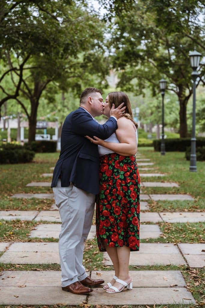 Engaged couple kisses on the tree-lined stone walkway at the Nelson-Atkins in Kansas City