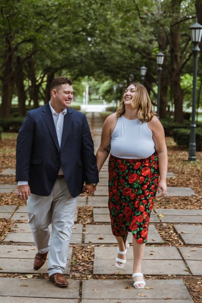 Engaged couple smiles at each other while walking the tree-lined linden walkway at the Nelson-Atkins in Kansas City
