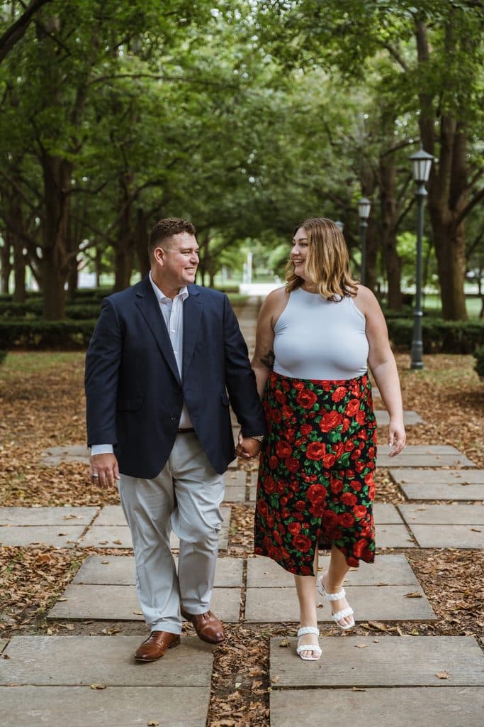 Engaged couple walks hand in hand under the linden trees at the Nelson-Atkins in Kansas City