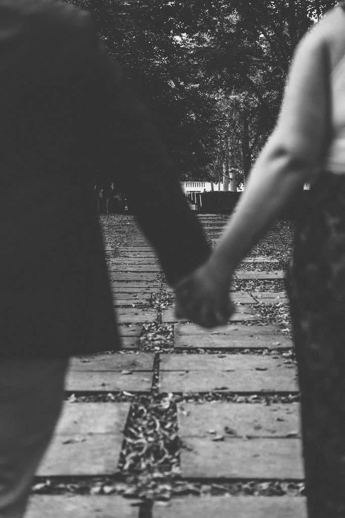 Black and white detail of an engaged couple holding hands as they walk a stone path at the Nelson-Atkins in Kansas City