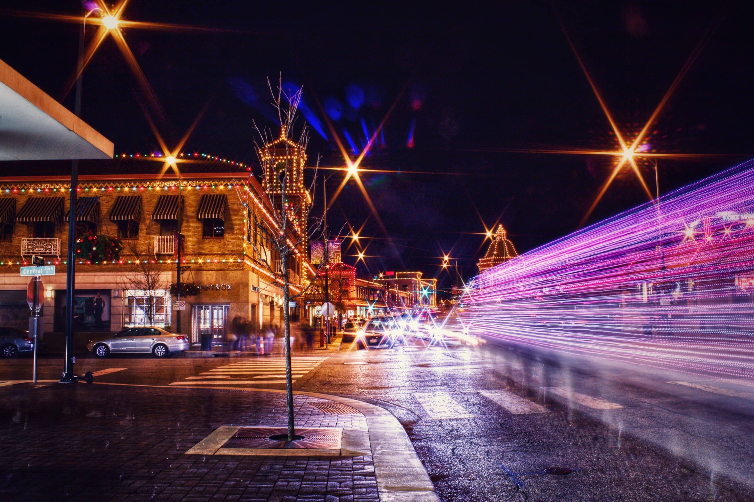 The Country Club Plaza in Kansas City outlined in holiday lights after dark, with light trails from passing traffic streaking across the wet street