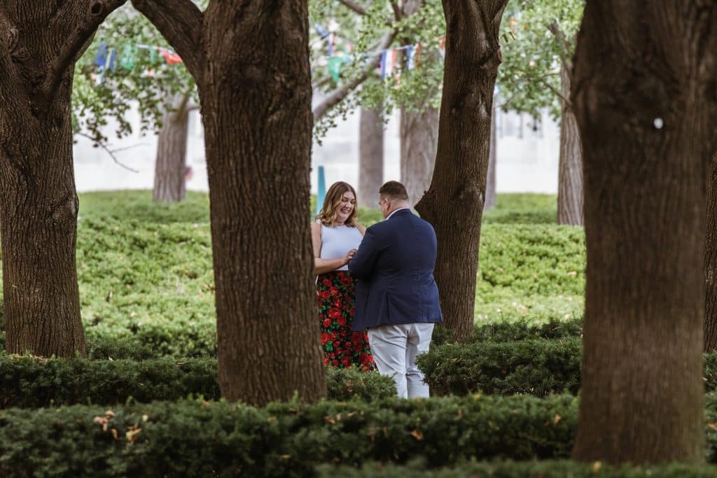 Man stands close to his girlfriend among the linden trees as he begins his proposal at the Nelson-Atkins in Kansas City
