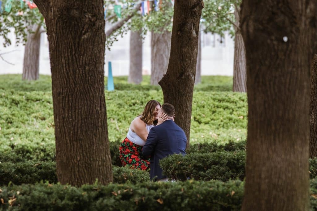 Newly engaged woman hugs her fiance as he kneels after she says yes at the Nelson-Atkins in Kansas City