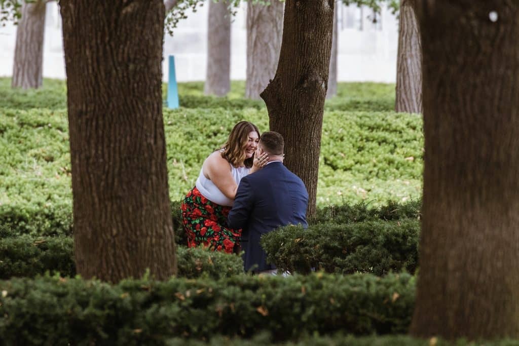 Woman kisses her new fiance as he kneels after the proposal at the Nelson-Atkins in Kansas City