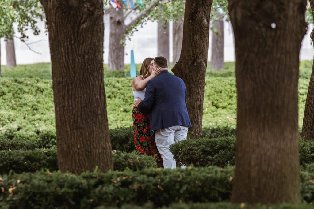 Groom-to-be stands and hugs his fiancee among the linden trees after proposing at the Nelson-Atkins in Kansas City