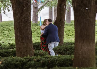Couple share a tight embrace among clipped hedges and tall tree trunks moments after he proposed